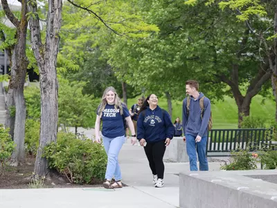 Three students wearing Oregon Tech shirts, walking across campus.